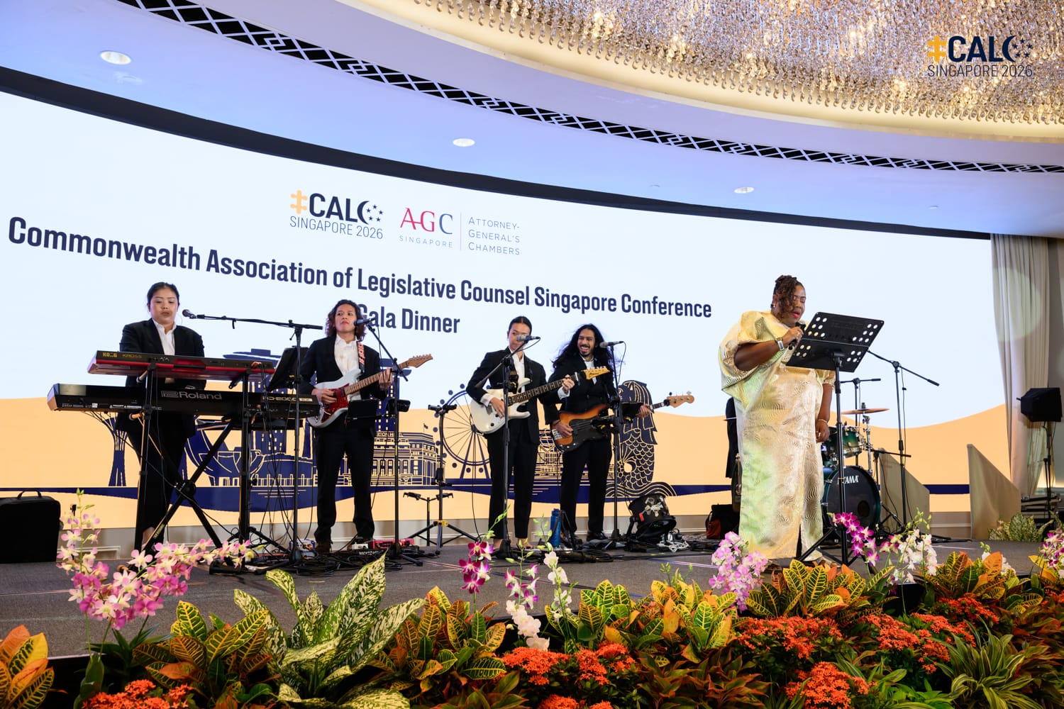 Ms Michelle Daley, incoming President of CALC, sings while the band 53A performs live on stage, at the Conference Gala Dinner, with the event backdrop displayed behind them.